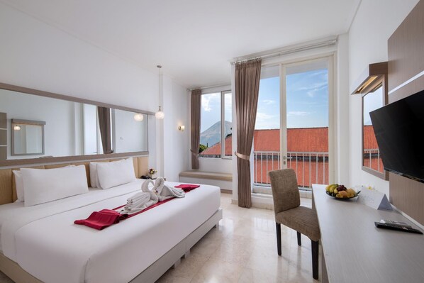 A hotel room with a bed, a desk with a bowl of fruit, a chair, and a TV. - Royal Trawas Hotel & Cottages (Trawas)