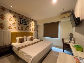 A hotel room with a bed, bedside table, desk, chair, and a TV mounted on the wall. - Jelita Tanjung Hotel (Murungpudak)