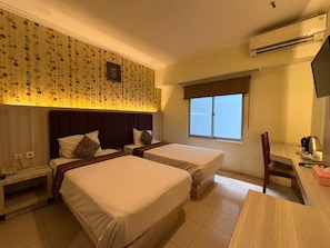 A hotel room with two beds, a desk, a chair, and a window. - Jelita Tanjung Hotel (Murungpudak)