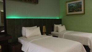 A hotel room with two single beds, a nightstand with a lamp, and a painting on the wall. - Sutanraja Hotel Kotamobagu (Kotamobagu)
