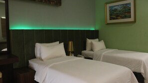 A hotel room with two single beds, a nightstand with a lamp, and a painting on the wall. - Sutanraja Hotel Kotamobagu (Kotamobagu)