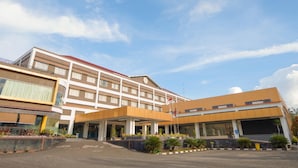 Un hotel de varios pisos con entrada cubierta, una bandera y un estacionamiento.