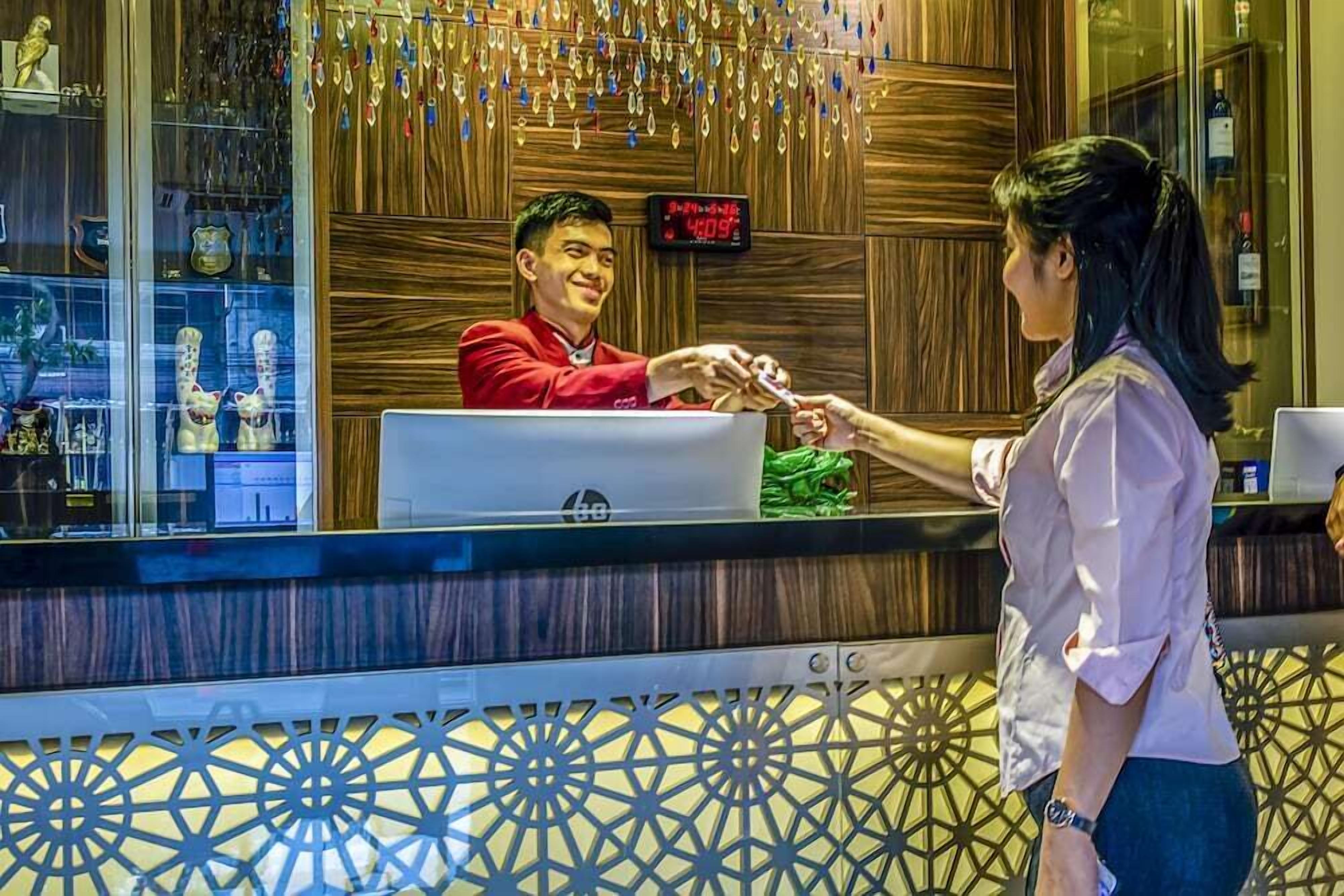 A hotel reception area with a wooden wall, a digital clock, and a glass display case with various items.
