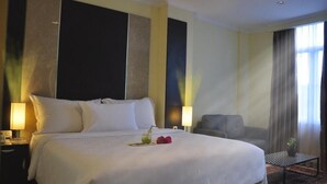 A hotel room with a large bed, two bedside tables, a chair, a small table, and a window with curtains. - Sunbreeze Hotel Jakarta (Jakarta)