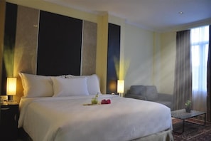 Une chambre d’hôtel avec un grand lit, deux tables de chevet, une chaise, une petite table et une fenêtre avec des rideaux.