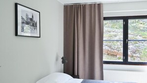 Una habitación de hotel con cama, ventana con cortinas, un cuadro enmarcado en la pared y un radiador.