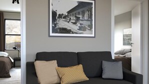 Una sala de estar moderna con un sofá oscuro, una fotografía en blanco y negro enmarcada en la pared y una mesita con un florero.