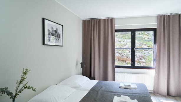 Een hotelkamer met een bed, een ingelijst schilderij aan de muur, een vaas met planten en een raam met gordijnen.