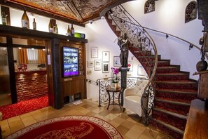 Un hall d’entrée avec un sol à carreaux, un coin bar avec des bouteilles exposées, un téléviseur, un escalier recouvert d’une moquette rouge et des tableaux encadrés accrochés aux murs.