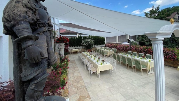 A statue of a historical figure, outdoor dining area with tables and chairs, and a pergola providing shade. - Woertz Schlosschen Zur Weinsteige (Stuttgart)