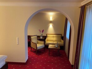 Ein Hotelzimmer mit rotem Teppich, einer Couch, einem Sessel, einem Tisch und einer Lampe.