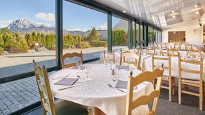 Een restaurant met gedekte tafels, grote ramen met uitzicht op de bergen en een modern interieur.