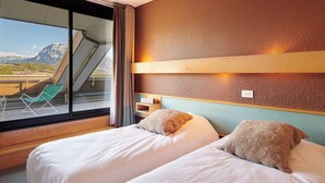 Een hotelkamer met twee bedden, een raam met uitzicht op bergen, een groene stoel en een houten plank.