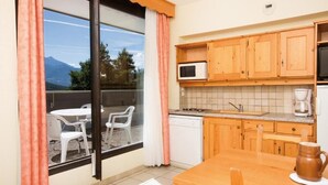 A kitchen with wooden cabinets, a microwave, a coffee maker, and a dining table with chairs. - Vacances Bleues Club Les Horizons Du Lac (Chorges)