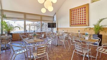 A restaurant with multiple tables and chairs, a TV screen, and a large window.
