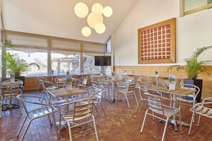 Ein Restaurant mit mehreren Tischen, Stühlen, einem Fernseher und einem großen Fenster.