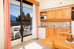 A kitchen with wooden cabinets, a microwave, a coffee maker, and a dining table with chairs. - Vacances Bleues Club Les Horizons Du Lac (Chorges)