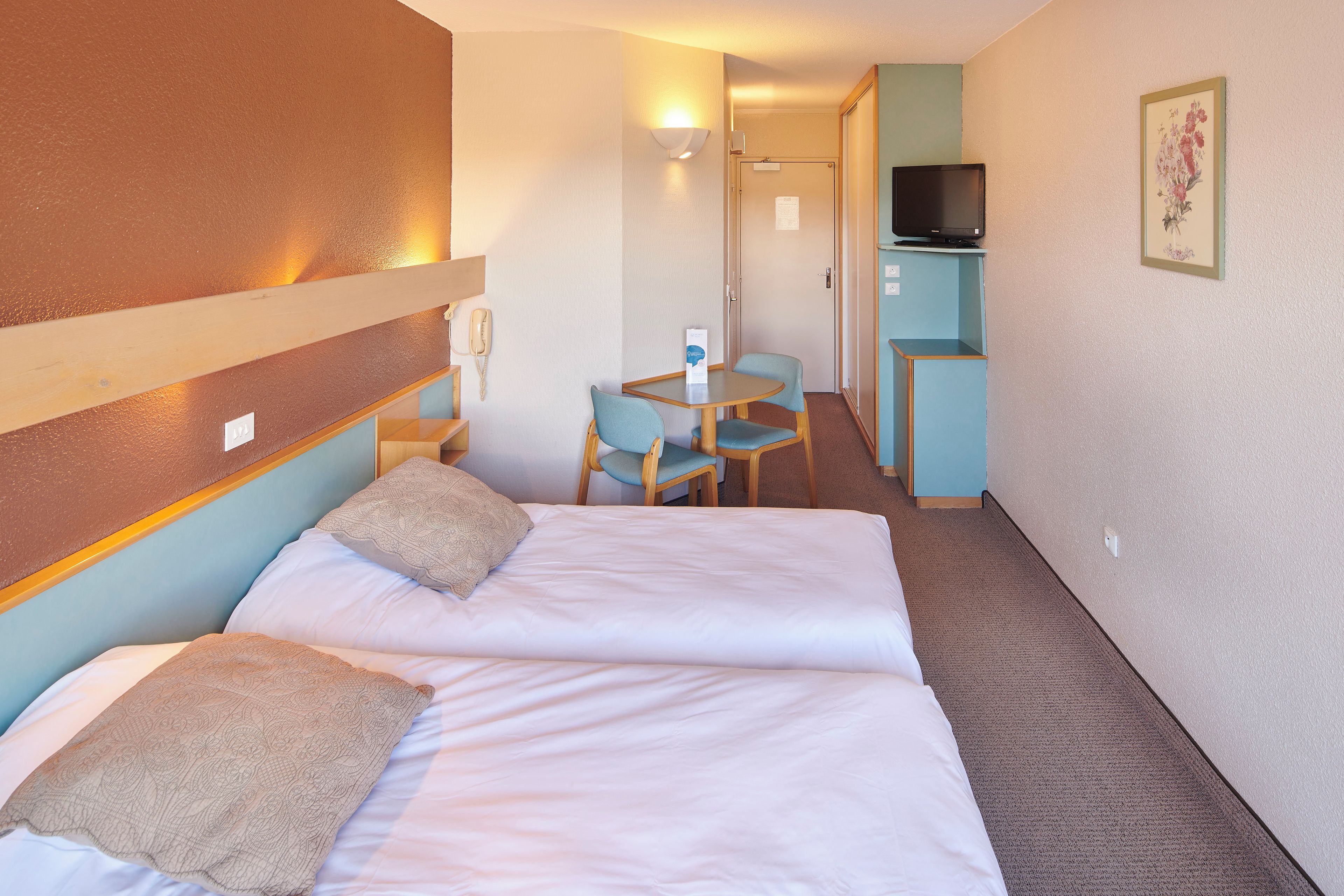 A hotel room with a bed, a desk, a chair, a television, and a small cabinet.