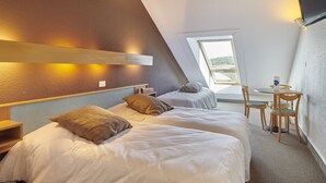Un dormitorio con dos camas, una mesita, una silla, un ventanal con vistas y un televisor montado en la pared.