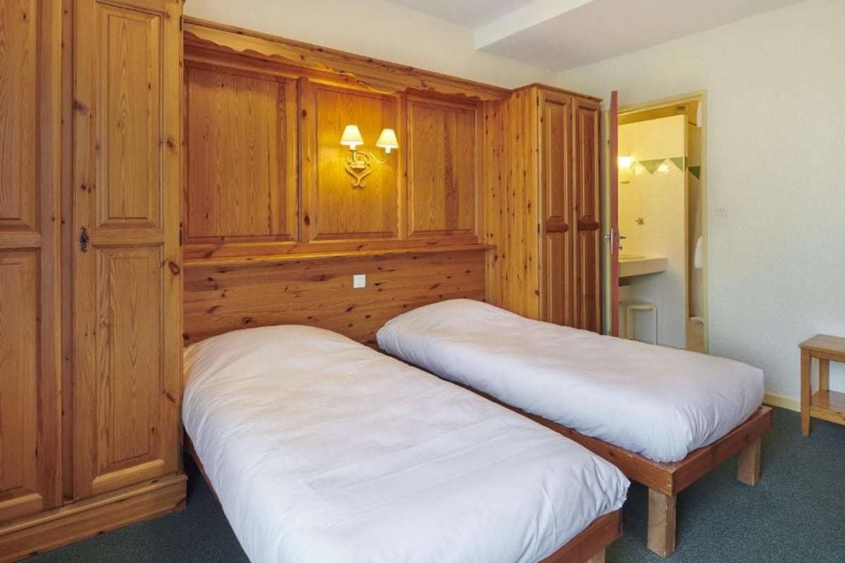 Una habitación con dos camas individuales, paneles de madera, un armario de madera y un espejo.