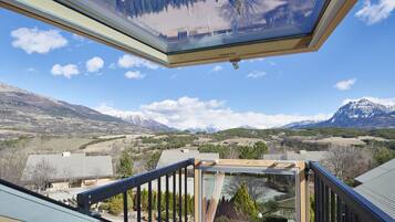 A view from a balcony with a skylight, overlooking a mountainous landscape with houses and a clear sky.