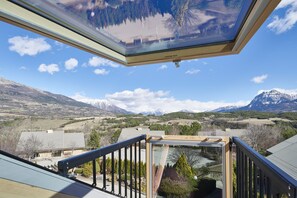 Blick vom Balkon mit Oberlicht auf eine gebirgige Landschaft mit Häusern und blauem Himmel.