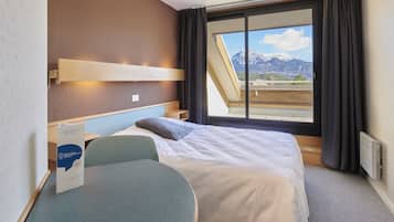 Habitación de hotel con cama, escritorio, silla y ventana con vistas a montañas, además de un cartel sobre el escritorio.