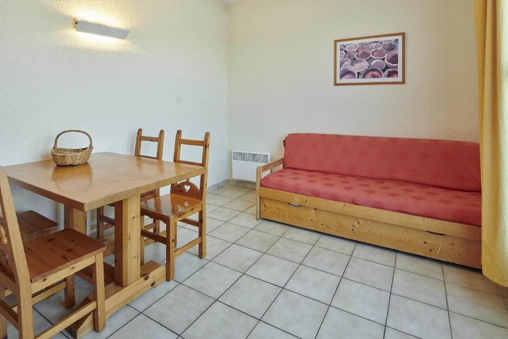 Una habitación con una mesa de comedor de madera, cuatro sillas, un sofá rojo, una lámpara de pared y un cuadro enmarcado.