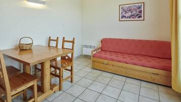 Una habitación con una mesa de comedor de madera, cuatro sillas, un sofá rojo, una lámpara de pared y un cuadro enmarcado.