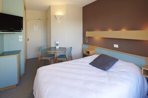 Ein Hotelzimmer mit Bett, Schreibtisch, Stuhl, Fernseher und Wandregal.