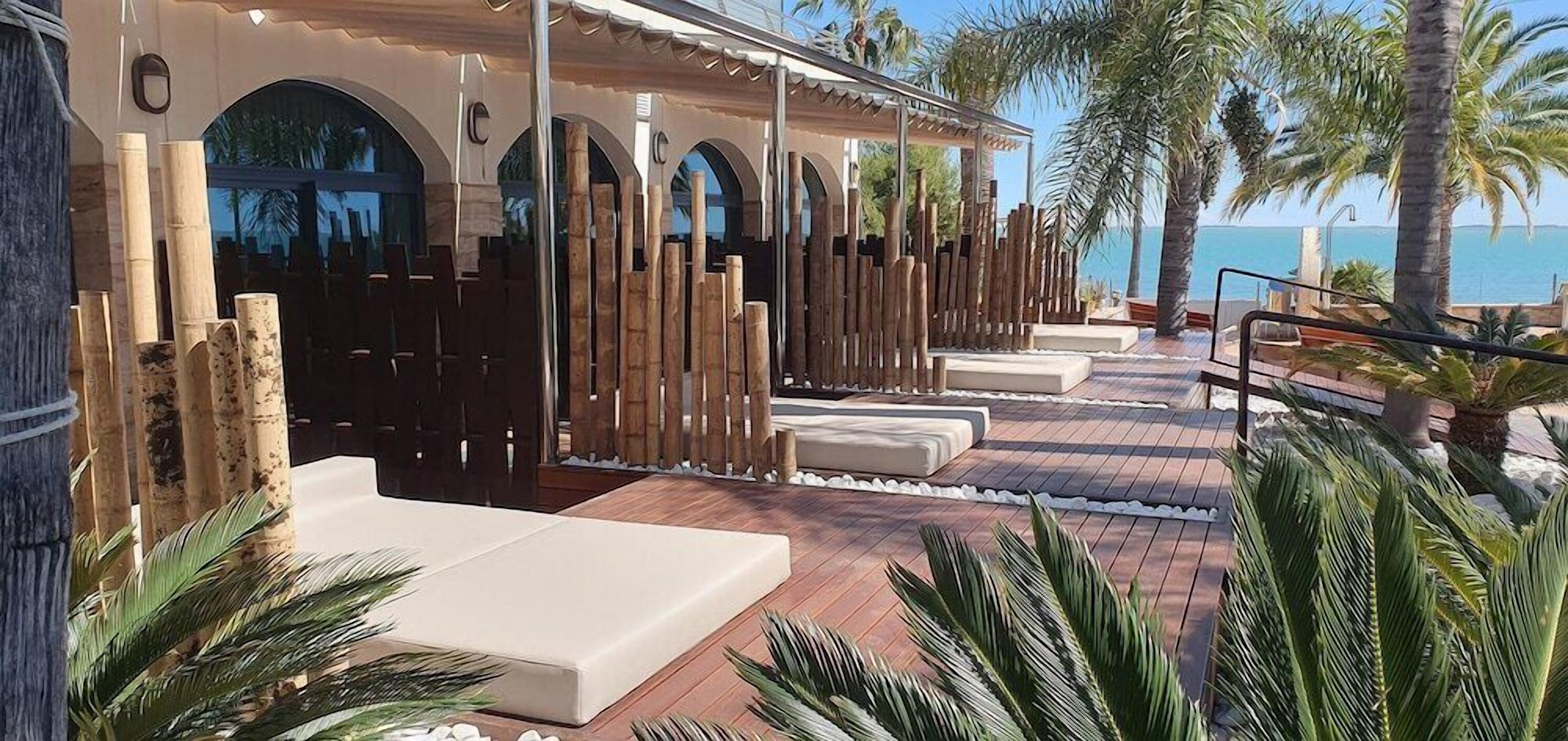 Un complexe hôtelier doté d’une terrasse en bois, de chaises longues et offrant une vue sur la mer.