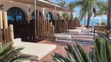 Un complexe hôtelier doté d’une terrasse en bois, de chaises longues et offrant une vue sur la mer.