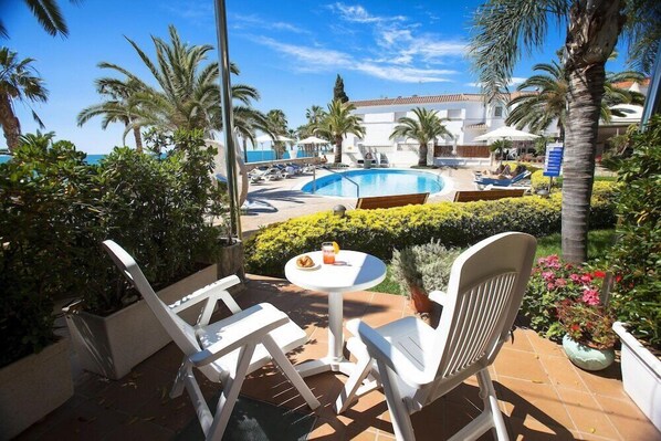 A poolside area with white chairs, a small table with a drink, and a view of the pool and beach. - Relais Du Silence Miami Mar (Sant Carles de la Rapita)