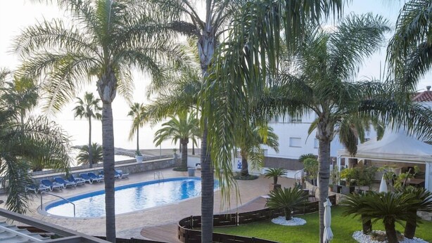 A pool area with palm trees, lounge chairs, and a white building in the background. - Relais Du Silence Miami Mar (Sant Carles de la Rapita)