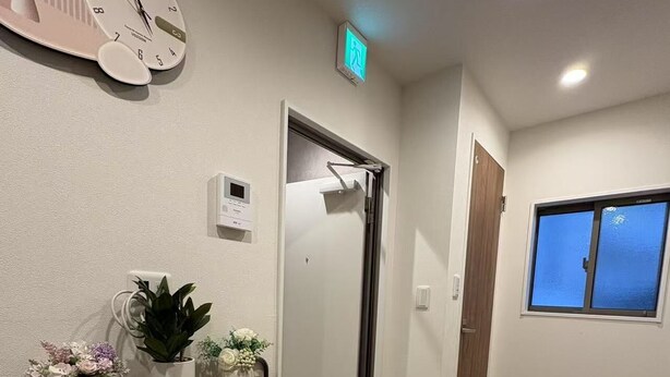 A reception area with a wooden counter, a wall clock, a potted plant, and a window with a view. - Minowa Station Hideaway - Breakfast + Free Coffee & Tea (台東区)