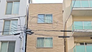 A multi-story building with a modern design, featuring a central entrance with glass doors and a staircase leading to the ground floor. - Minowa Station Hideaway - Breakfast + Free Coffee & Tea (台東区)