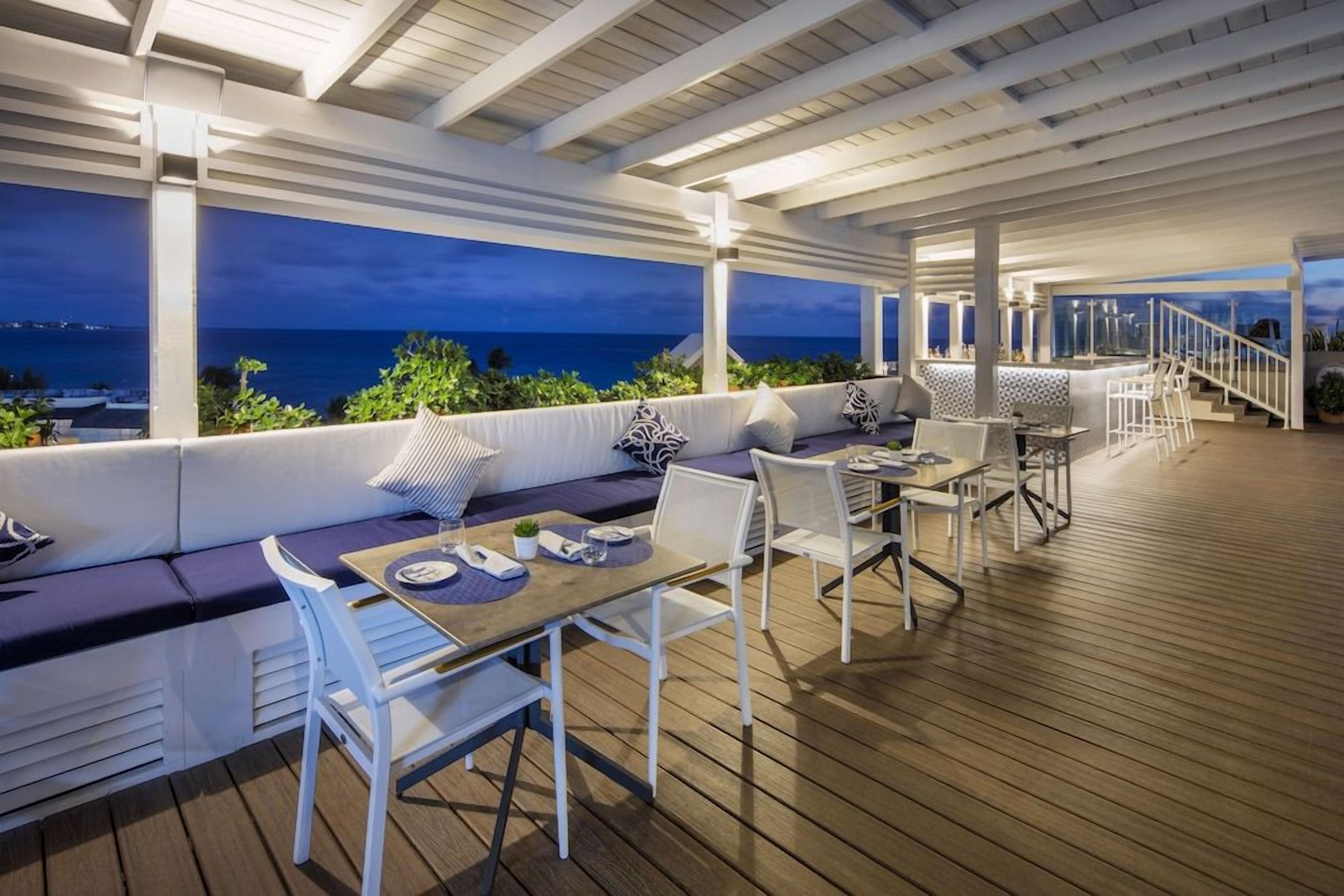 An outdoor seating area with a view of the ocean, a wooden deck, and a bar area.