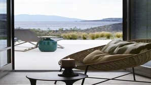 Un balcón con una silla de mimbre, una mesita con una vela y vistas al mar y a las montañas.