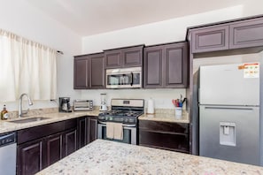A kitchen with dark brown cabinets, a stainless steel refrigerator, a microwave, a stove, a sink, and a coffee maker. - Casa Los Monos | Where Nature Meets Comfort (Nosara)