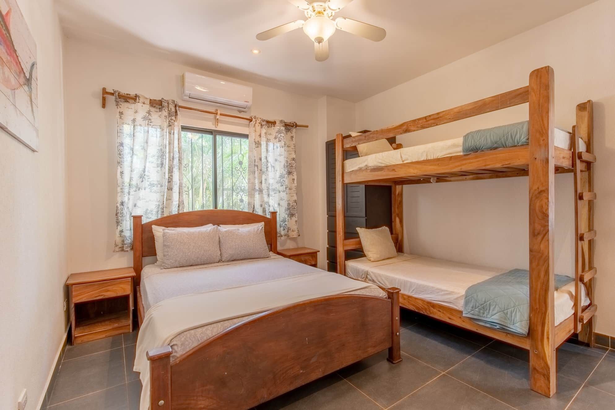 Un dormitorio con una cama individual, una litera, una ventana con cortinas, un aire acondicionado y un ventilador de techo.
