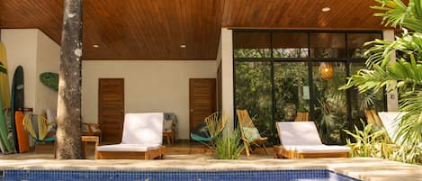 Zona de piscina con sillas de descanso, techo de madera y vistas al exterior.