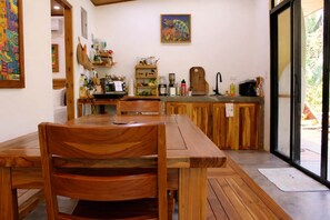 A wooden dining table with chairs, a kitchen area with wooden cabinets, a sink, and a painting on the wall. - Turtle House | Jungle Retreat w/ Pool in Nosara (Nosara)