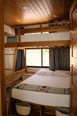 Ein Schlafraum mit Etagenbetten, einem Fenster, Holzwänden und einem Bett mit einem gemusterten Bettbezug.