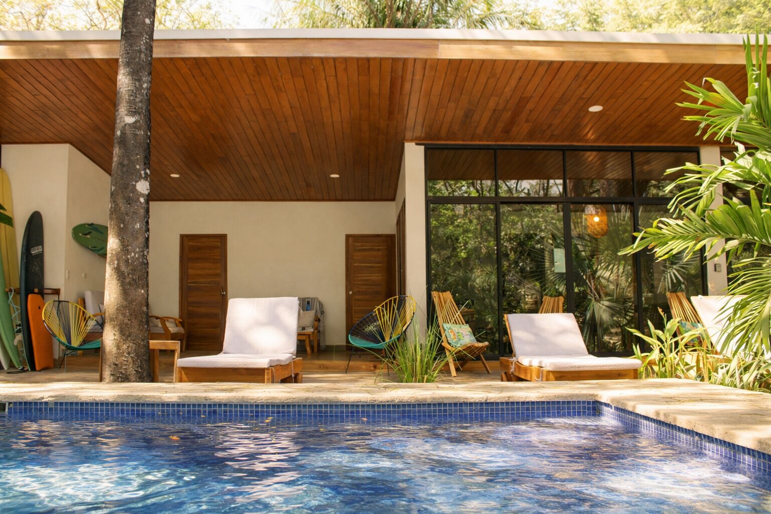 Zona de piscina con sillas de descanso, techo de madera y vistas al exterior.