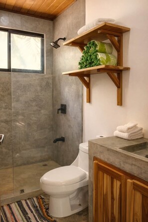 Ein Badezimmer mit Dusche, Toilette und Holzregalen über dem Waschbecken.