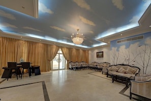 Um hall amplo com um candelabro, área de refeições, sofás e um mural com árvores na parede.