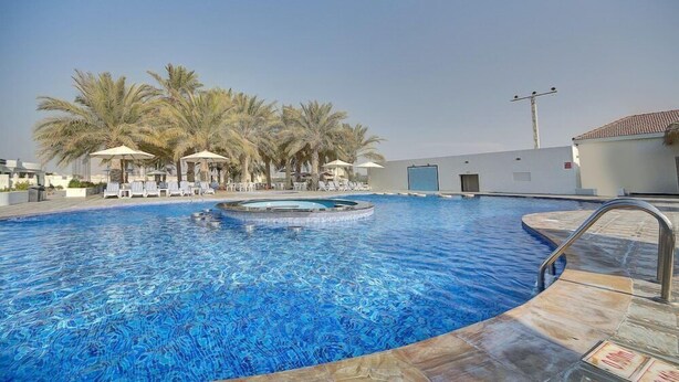 A swimming pool with lounge chairs and umbrellas, surrounded by palm trees. - Royal Residence Resort (Umm al Quwain)