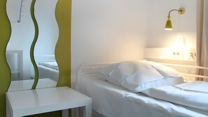 Une pièce comprenant un lit, une petite table blanche, un miroir avec un cadre vert et une lampe fixée au mur.
