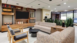 A modern living room with a large flat-screen TV, comfortable seating, and a bookshelf. - Drury Plaza Hotel Columbus Downtown (Columbus)