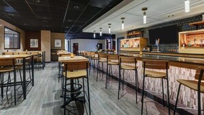 A restaurant with multiple tables and chairs, a bar area with shelves of bottles, and a large screen on the wall. - Drury Plaza Hotel Columbus Downtown (Columbus)